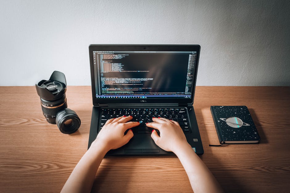 A white ceramic mug with black speckled pattern and a rounded handle placed on a dark surface in front of an open laptop displaying lines of computer code with various highlighted syntax. The backgrou