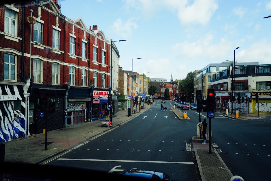 A daytime street scene in Finsbury Park showing a row of mixed-use brick and modern buildings on the left side, with shopfronts featuring large windows, some with graffiti-style murals, and signage fo