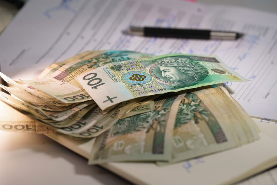 A close-up view of multiple UK banknotes, including 20 and 100-pound notes, placed on top of papers and documents related to home relocation, with a black pen and a cardboard box partially visible in